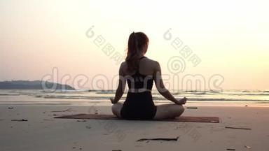 背面的观点，女人练习瑜伽，莲花姿势，冥想与暑假在海滩上。